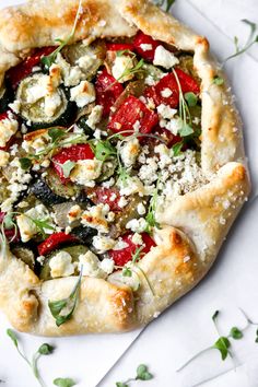 a pizza topped with lots of toppings on top of a white plate next to green leaves