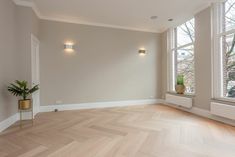 an empty room with two large windows and wooden floors in the center is a potted plant