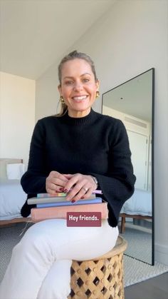 a woman sitting on a stool with books in her lap and smiling at the camera