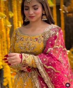 a woman in a yellow and pink outfit looking down at her cell phone while wearing gold jewelry