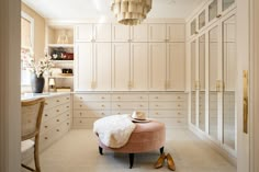 a room with white cabinets and a pink ottoman in the middle of it, along with a chandelier hanging from the ceiling