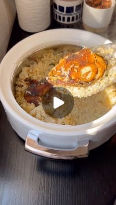 a white bowl filled with rice and meat on top of a wooden table next to cups