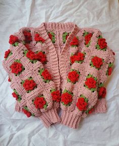 two pink knitted sweaters with red roses on them sitting on a white sheet