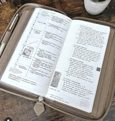 an open book sitting on top of a wooden table next to a cup and pen