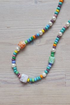 a multicolored beaded necklace on a wooden table with an orange and white flower