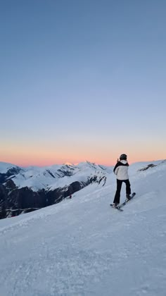 a person riding a snowboard on top of a snow covered slope with mountains in the background