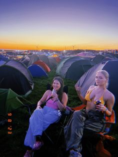 two women sitting on chairs in front of tents at sunset with the sun setting behind them