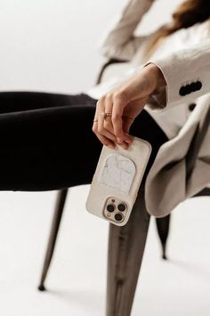 a woman sitting on a chair holding a cell phone in one hand and a camera in the other