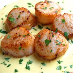 seared scallops with sauce and parsley on a yellow plate, ready to be eaten