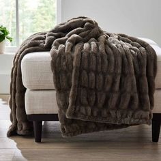 a couch with a blanket on top of it in front of a window and potted plant