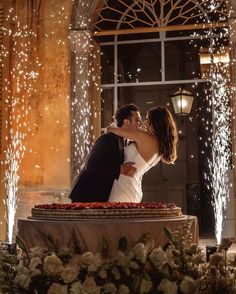 a bride and groom kissing in front of a fountain surrounded by lights at their wedding reception