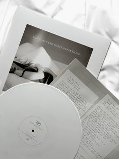 a white cd case sitting on top of a bed next to an open book and papers