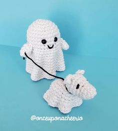 two small crocheted white dogs on a blue background, one is holding a leash