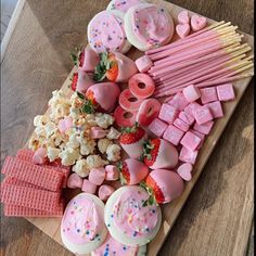 a wooden tray topped with lots of pink and white treats next to marshmallows