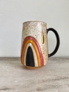 a ceramic coffee mug with a rainbow design on the outside and gold trimmings