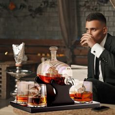 a man in a suit sitting at a table with three glasses and a decanter