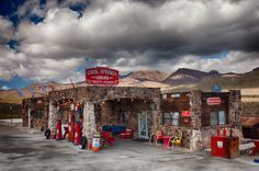 an old fashioned gas station with mountains in the backgrouds and cloudy skies