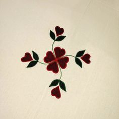 a white table cloth with red flowers and green leaves on the edge, embroidered onto it