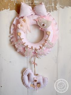 a pink wreath hanging from the side of a door with two teddy bears attached to it