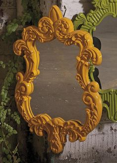 a yellow mirror sitting on the side of a wall next to a green vine covered wall