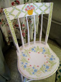 a white chair with flowers painted on it's back and seat is sitting in front of a curtain