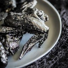 some black food on a white plate with silver flakes and crinkled cloth