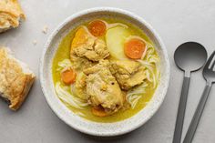 a bowl of chicken noodle soup with two spoons next to it on a table