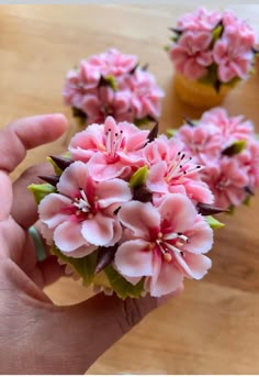 small pink flowers sitting on top of a wooden table next to a person's hand