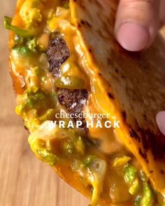 a hand holding a tortilla with cheese and green peppers on it, over a wooden table