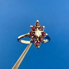 a diamond and ruby flower ring is shown against a bright blue background with a gold stick