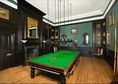 a pool table in the middle of a room with green walls and wood flooring