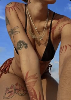 a woman with tattoos on her body sitting in front of a blue sky and clouds