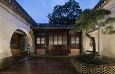 an outdoor courtyard at night with potted trees in the foreground and tiled walkway