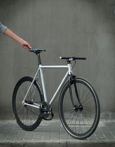 a person is holding the handlebars on a silver bicycle against a gray wall