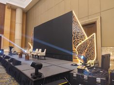 a stage set up for a conference with chairs and lights on the side, in front of a large screen