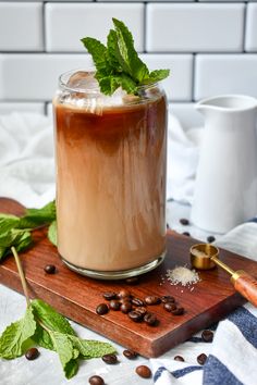 a glass filled with iced coffee on top of a wooden cutting board next to beans and mint