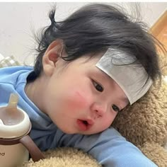 a baby laying on top of a teddy bear next to a bottle with a bandage on it's head