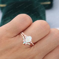 a woman's hand holding an opal and diamond ring