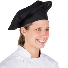 a woman wearing a black chef's hat and smiling at the camera while standing in front of a white background