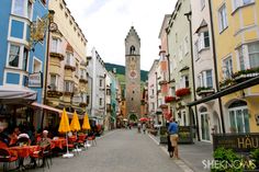 people are sitting at tables in the middle of an alleyway with colorful buildings on both sides