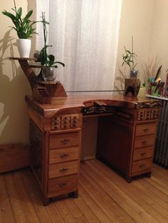 a wooden desk with two potted plants sitting on it's top, in front of a window