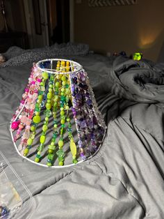 a lamp shade made out of beads and glass beads on a bed with a gray comforter