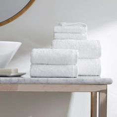 a stack of white towels sitting on top of a wooden table next to a mirror