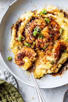 a white plate topped with mashed potatoes covered in shrimp and green onions next to a fork