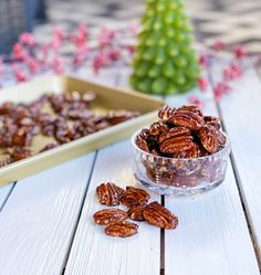 a bowl full of pecans sitting on top of a wooden table next to a tray of pecans