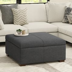 a living room with a couch, ottoman and coffee table in front of a window