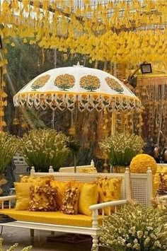 a yellow couch sitting under an umbrella in a room filled with potted plants and flowers