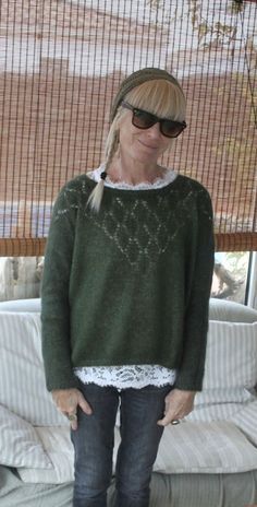 a woman standing in front of a couch wearing a green sweater and black jeans with white lace trim