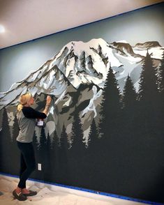 a woman is painting a mountain scene on the wall