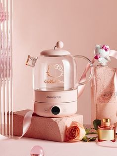 a pink hello kitty tea kettle next to some flowers